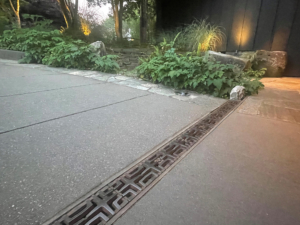 Decorative cast iron trench grate in Carbochon pattern, installed in concrete driveway.