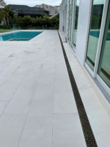 Decorative cast bronze trench grate in Greek Key pattern installed on pool patio