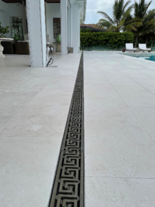 Decorative cast bronze trench grate in Greek Key pattern installed on pool patio