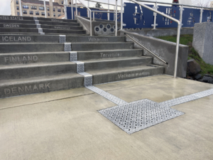 Cast aluminum trench drain grates in decorative Interlaken pattern, installed down center of concrete staircase