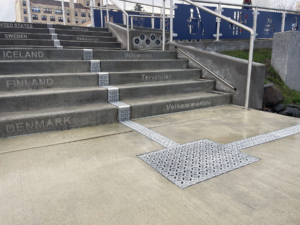 Cast aluminum trench drain grates in decorative Interlaken pattern, installed down center of concrete staircase