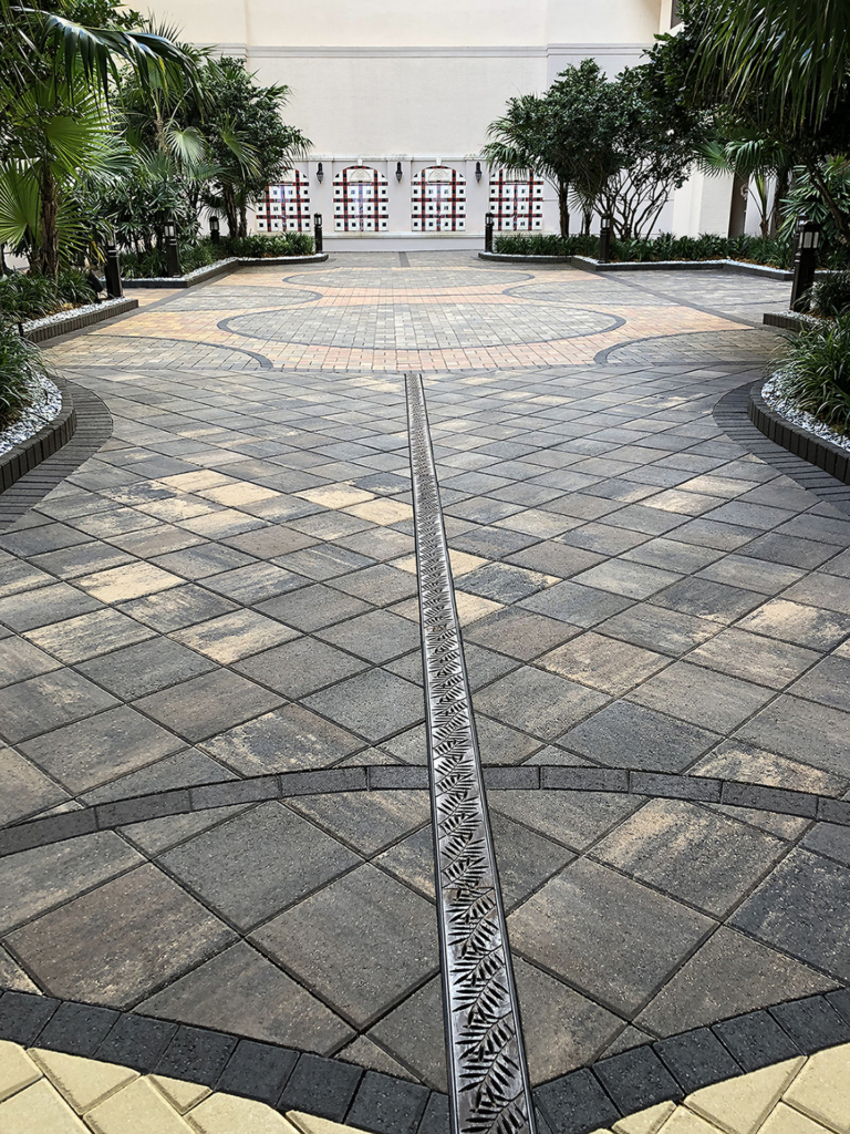 Cast iron trench drain grates with decorative Locust pattern, installed in driveway with pavers