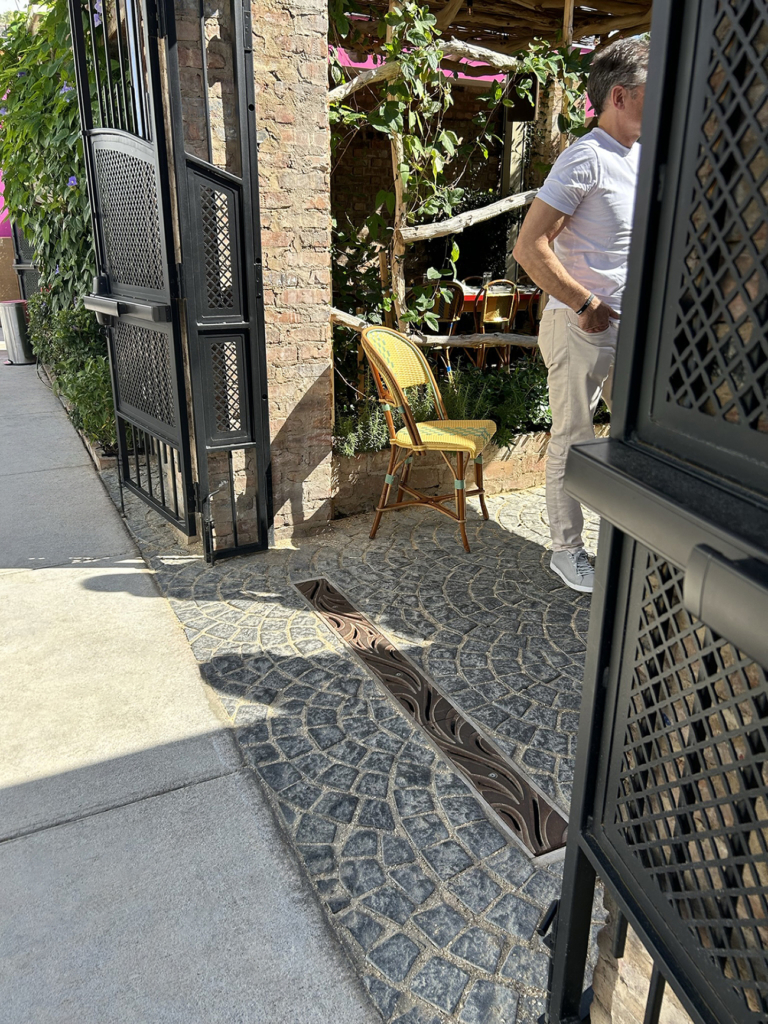 Raw cast iron trench grate in decorative Minnione pattern from Iron Age Designs. Located in outdoor restaurant courtyard.
