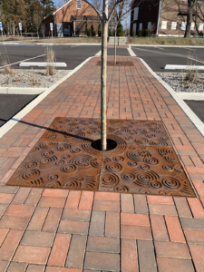 Cast iron tree grate with decorative Oblio pattern, surrounded by brick pavers