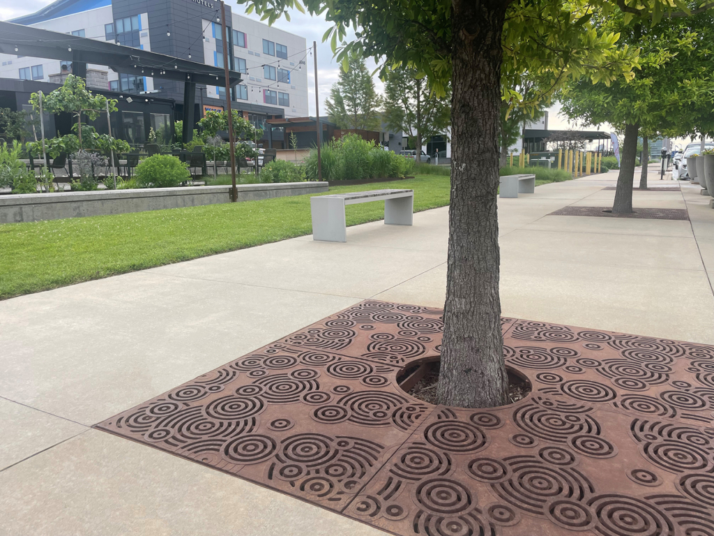 Cast iron tree grate in decorative Oblio pattern from Iron Age Designs. Installed in community plaza.