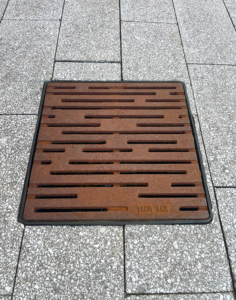 Cast iron catch basin grate in decorative Rain pattern from Iron Age Designs, set in concrete pavers.