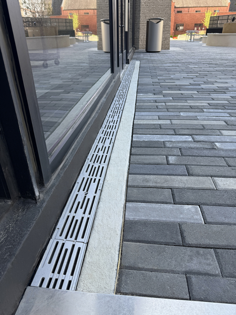 Cast iron trench grate in decorative Rain pattern from Iron Age Designs. Installed in building entryway.