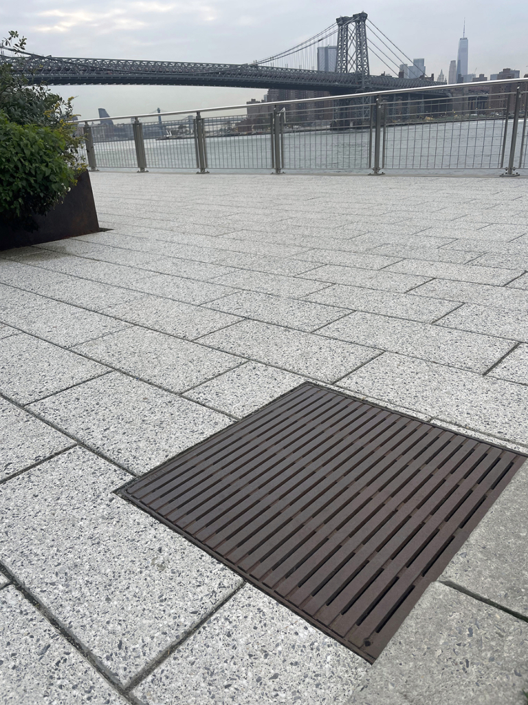 Cast iron drain grates in linear Regular Joe pattern, with Brooklyn Bridge in the background