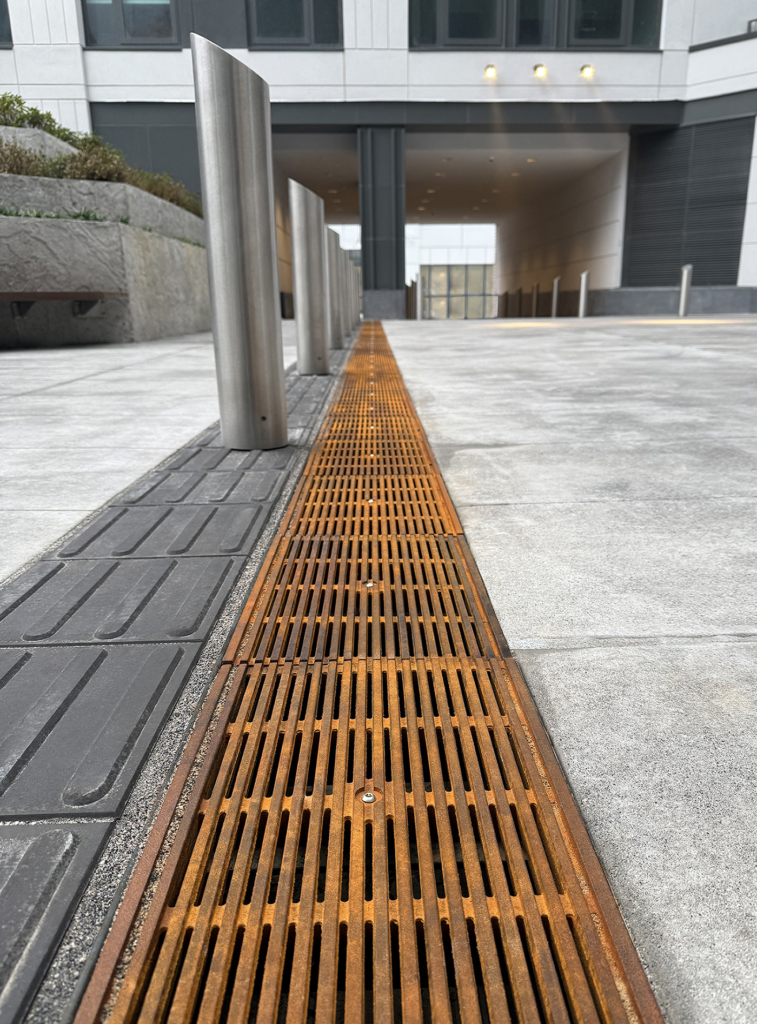 Cast iron Que trench grates by Iron Age Designs installed next to directional wayfinding tiles.
