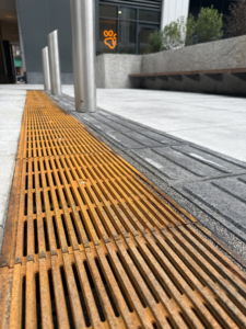 Cast iron Que trench grates by Iron Age Designs installed next to directional wayfinding tiles.