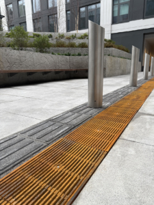 Cast iron Que trench grates by Iron Age Designs installed next to directional wayfinding tiles.