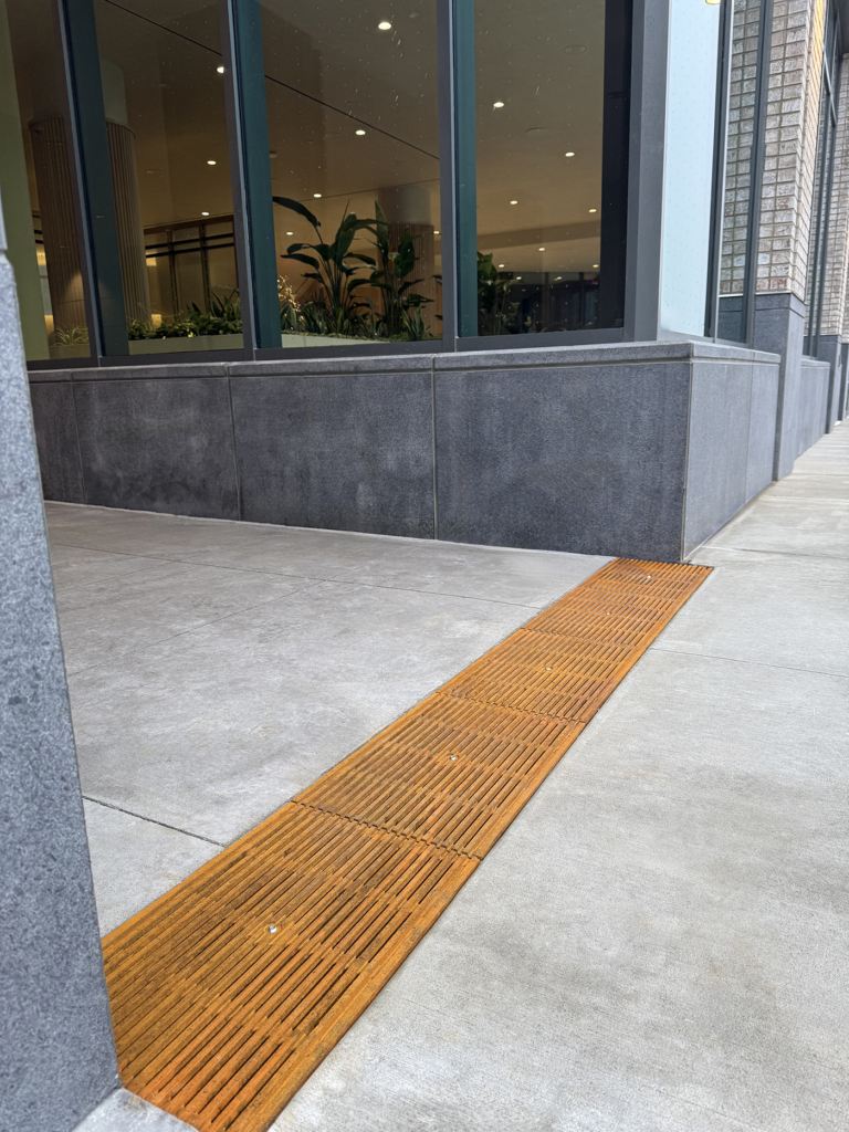 Cast iron Que trench grates by Iron Age Designs installed near building entryway.