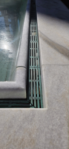 Cast bronze trench grates in water feature, aged 7 years, showing verdigris finish. Que pattern by Iron Age Designs.