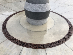 Cast iron radius trench drain grates in decorative Oblio pattern, installed around water feature