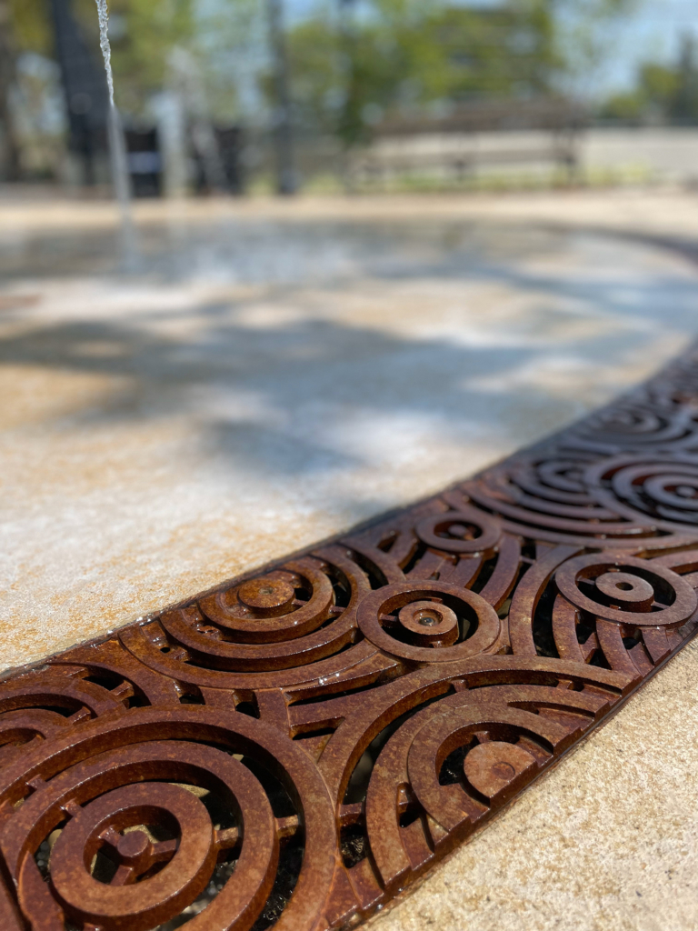 Cast iron radius trench grate in decorative Oblio pattern from Iron Age Designs. Installed in splash park.