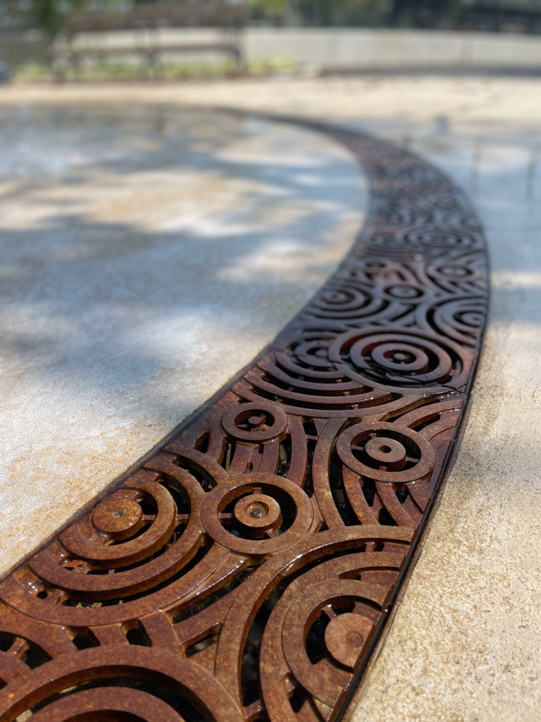 Cast iron radius trench grate in decorative Oblio pattern from Iron Age Designs. Installed in splash park.