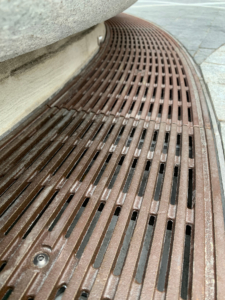 Decorative cast bronze radius trench grates in Que pattern surrounding circular planter