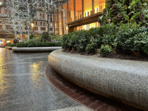 Cast iron radius drain grate in linear Que pattern, shown at base of large planters in One Vanderbilt Plaza