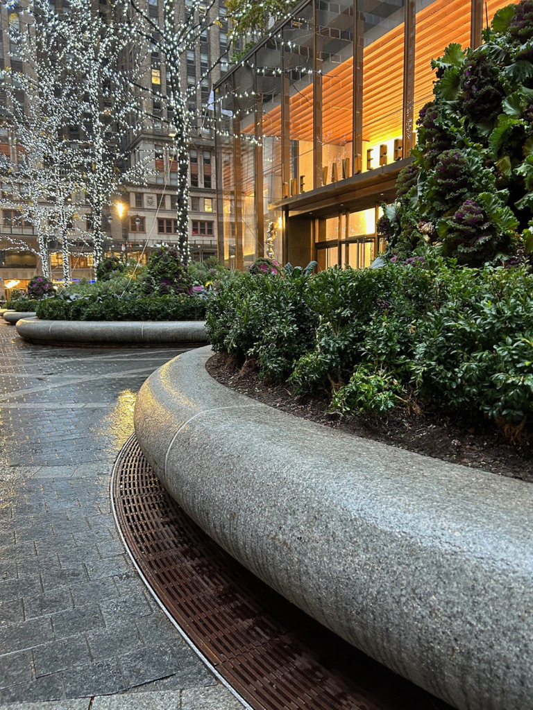 Cast iron radius drain grate in linear Que pattern, shown at base of large planters in One Vanderbilt Plaza