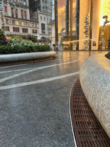 Cast iron radius drain grate in linear Que pattern, shown at base of large planters in One Vanderbilt Plaza