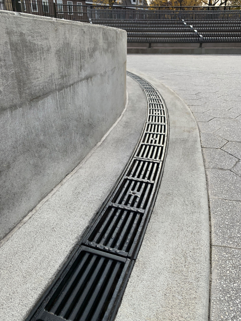 Cast iron radius trench drain grates in a linear Que pattern, black powder coat finish.