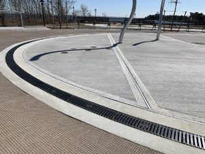 Cast iron radius trench grate with powder coat finish in ellipse shape around a spray park