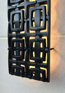 Cast iron, powder coated Carbochon drain grate shown used as lighting sconce on outside of building