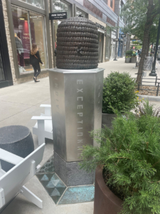 Cast bronze bee skep sculpture on metal base with decorative cast bronze tiles at base.