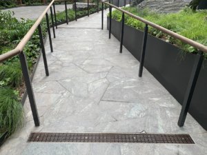 Decorative cast iron trench grate at entry of walkway with pavers and railing