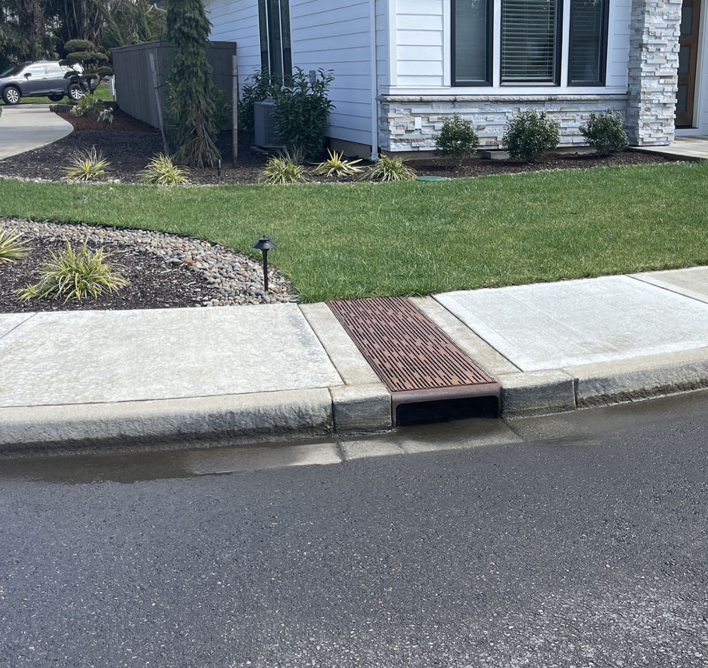 Cast iron curb inlet with decorative Rain trench drain grates cutting across the sidewalk