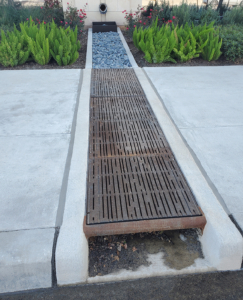 Curb Inlet with decorative grates covering runnel across sidewalk to bioswale on other side.
