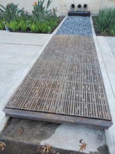 Curb Inlet with decorative grates covering runnel across sidewalk to bioswale on other side.