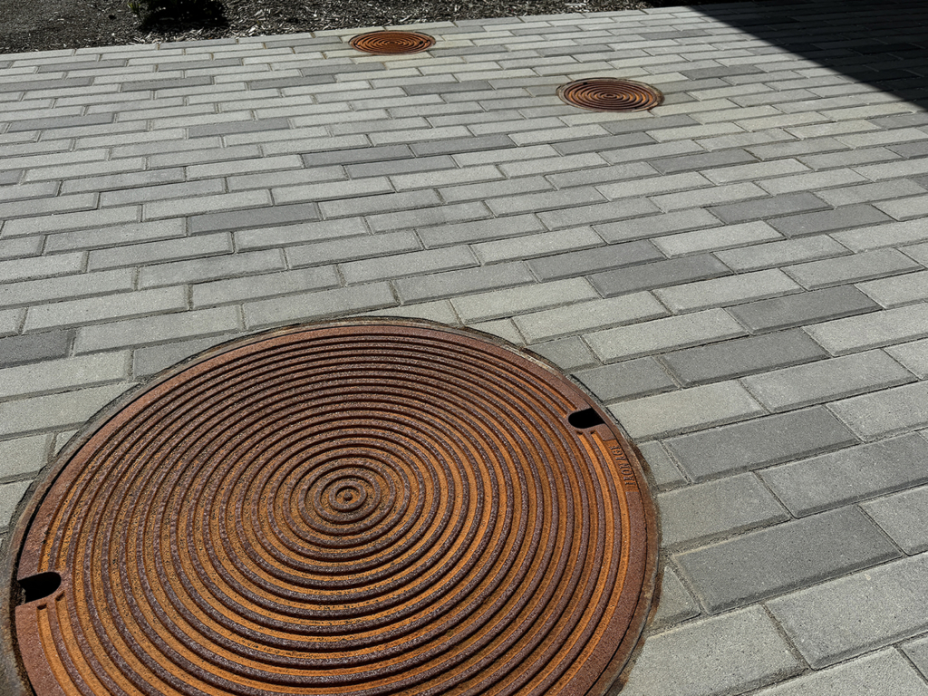 Raw cast iron manhole covers in decorative Bullseye pattern from Iron Age Designs. Installed in courtyard with pavers.
