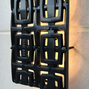 Cast iron, powder coated Carbochon drain grate shown used as lighting sconce on outside of building