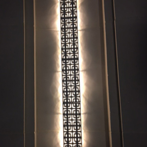 Cast iron, powder coated Carbochon drain grate shown used as lighting sconce on outside of building