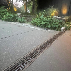 Decorative cast iron trench grate in Carbochon pattern, installed in concrete driveway.