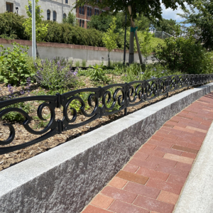 Decorative planter in road median on college campus, surrounded by custom cast iron planter fence.