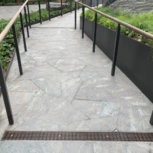 Decorative cast iron trench grate at entry of walkway with pavers and railing