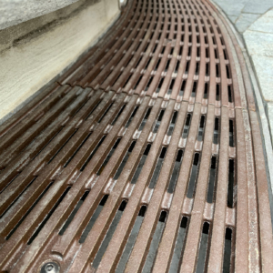 Decorative cast bronze radius trench grates in Que pattern surrounding circular planter