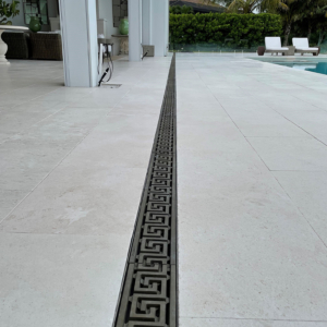 Decorative cast bronze trench grate in Greek Key pattern installed on pool patio