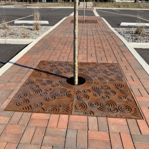 Cast iron tree grate with decorative Oblio pattern, surrounded by brick pavers