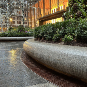 Cast iron radius drain grate in linear Que pattern, shown at base of large planters in One Vanderbilt Plaza