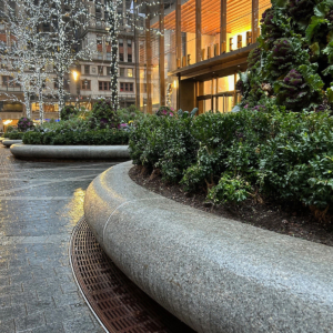 Cast iron radius drain grate in linear Que pattern, shown at base of large planters in One Vanderbilt Plaza