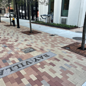 Cast iron tree grate with light hole cut-outs in linear Rain pattern, set in plaza of multicolored pavers